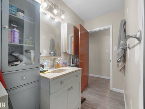 Bathroom vanity with integrated sink, light wood-finish flooring, and a wall-mounted light fixture - 12002 48 Street Nw, Edmonton, AB 