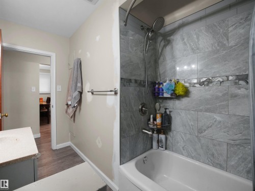 Bathtub with tiled surround featuring a decorative accent band and a wall-mounted showerhead - 12002 48 Street Nw, Edmonton, AB 