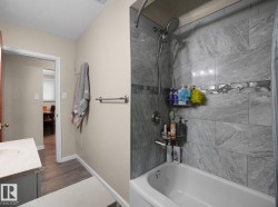 Bathtub with tiled surround featuring a decorative accent band, chrome shower fixtures, and a vanity with a light-colored countertop - 