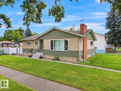 Exterior featuring green horizontal siding, stucco details, a brick chimney, and a concrete sidewalk - 