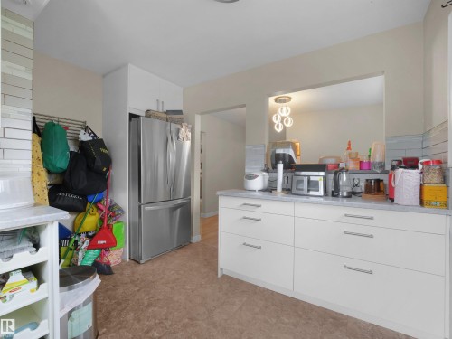 White cabinetry with brushed nickel hardware, light-toned countertops, and a stainless steel refrigerator - 12002 48 Street Nw, Edmonton, AB 