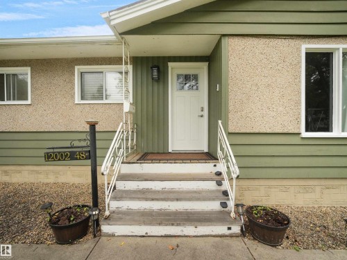 Entryway featuring a white paneled door with glass inserts, exterior wall sconce, and a wood step porch with white metal handrails - 12002 48 Street Nw, Edmonton, AB 