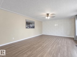 Wood-finish flooring, textured accent wall, ceiling fan with integrated lighting, and crown molding - 