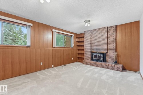 Brick fireplace with wood-burning insert, integrated shelving, wood paneling, and two windows - 11311 Malmo Road Nw, Edmonton, AB 