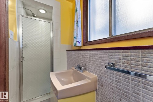 Wall-mounted sink with chrome fixtures, textured wall tiling, and a frosted window with a wood frame - 11311 Malmo Road Nw, Edmonton, AB 