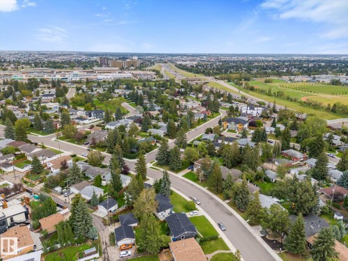 Established neighborhood with mature trees, residential street, curved roads, distant commercial buildings, and open green spaces - 11311 Malmo Road Nw, Edmonton, AB 