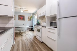 Kitchen featuring white cabinetry, dark countertops, wood-finish flooring, white appliances, and a dining area with a ceiling fan - 