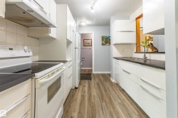 Galley kitchen featuring wood-finish flooring, white cabinetry with silver-tone hardware, and dark countertops - 
