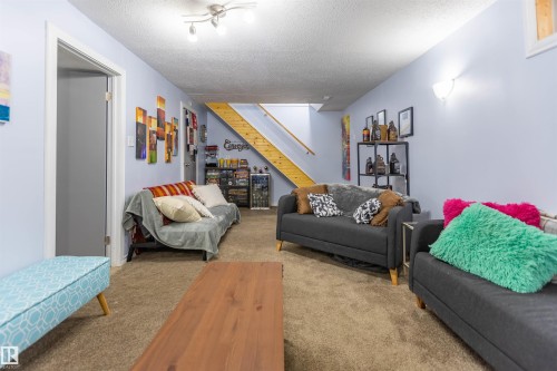 Spacious room featuring light blue walls, brown carpeting, an exposed wood-finish staircase, and ceiling-mounted track lighting - 13323 47 Street Nw, Edmonton, AB - Indoor Photo Showing Other Room