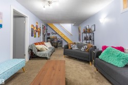 Spacious room featuring light blue walls, brown carpeting, an exposed wood-finish staircase, and ceiling-mounted track lighting - 