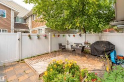 Private backyard featuring an elevated wood-finish deck, paver patio, white privacy fencing, and mature landscaping - 