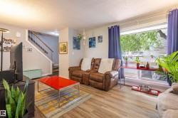 Bright living area with wood-finish flooring, a prominent window, and a staircase featuring a wood handrail - 
