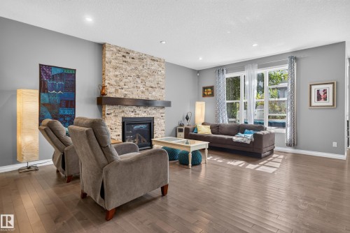 Stone-clad fireplace with wood-beam mantle, recessed lighting, wood-finish flooring, and expansive windows - 22933 94A Avenue Nw, Edmonton, AB 