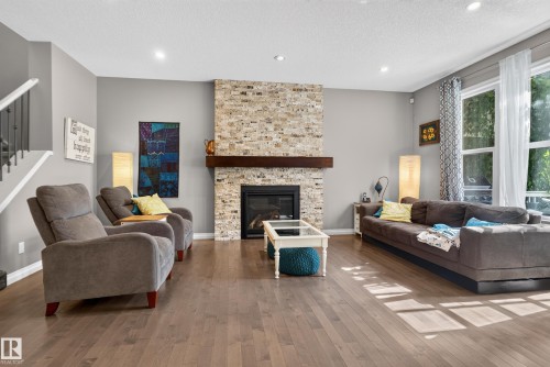 Hardwood flooring throughout, stone-finish fireplace with wood mantel, large windows, recessed lighting, and a staircase with white risers and dark handrail - 22933 94A Avenue Nw, Edmonton, AB 