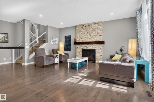 Wood-finish flooring throughout, a stone-clad fireplace with a wood mantel, and recessed ceiling lighting - 22933 94A Avenue Nw, Edmonton, AB 