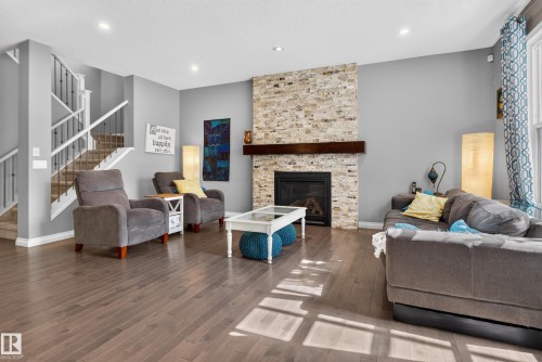 Wood-finish flooring throughout, stone-clad fireplace with wood mantel, and a staircase featuring white risers and dark metal spindles - 22933 94A Avenue Nw, Edmonton, AB 