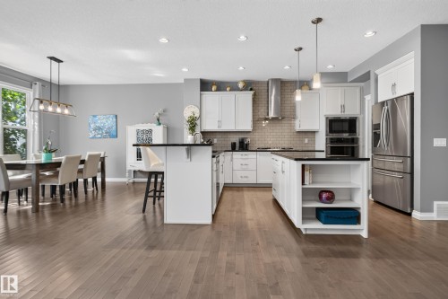 Open-concept living area with wood-finish flooring, white cabinetry, dark countertops, and stainless steel appliances - 22933 94A Avenue Nw, Edmonton, AB 