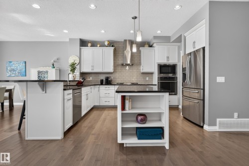 Kitchen featuring white cabinetry, black countertops, stainless steel appliances, a tile backsplash, and wood-finish flooring - 22933 94A Avenue Nw, Edmonton, AB 