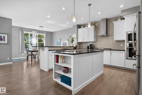 Kitchen featuring wood-finish flooring, white cabinetry, dark countertops, a subway tile backsplash, and stainless steel appliances - 22933 94A Avenue Nw, Edmonton, AB 