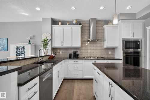 Expansive kitchen featuring white cabinetry, dark countertops, a subway tile backsplash, stainless steel appliances, and wood-finish flooring - 22933 94A Avenue Nw, Edmonton, AB 