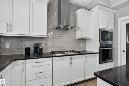 White cabinetry with brushed nickel hardware, gray subway tile backsplash, built-in stainless steel oven and microwave, stainless steel gas cooktop, and dark countertop surfaces - 22933 94A Avenue Nw, Edmonton, AB 