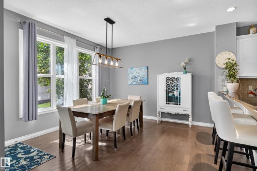 Dining area with wood-finish flooring, a linear chandelier, and ample natural light through large windows - 22933 94A Avenue Nw, Edmonton, AB 