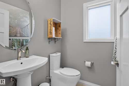 Pedestal sink with a polished chrome faucet, round frameless mirror, white two-piece toilet, and a window with white trim - 22933 94A Avenue Nw, Edmonton, AB 