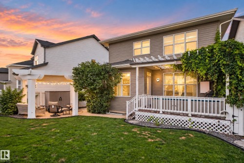 Expansive backyard featuring a manicured lawn, a white pergola-covered patio, and a raised wood-finish deck with white railings - 22933 94A Avenue Nw, Edmonton, AB 