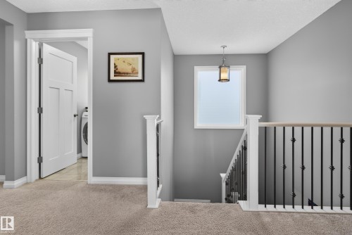 Staircase featuring a white balustrade with black decorative iron spindles, wood-finish handrail, and pendant light fixture - 22933 94A Avenue Nw, Edmonton, AB 