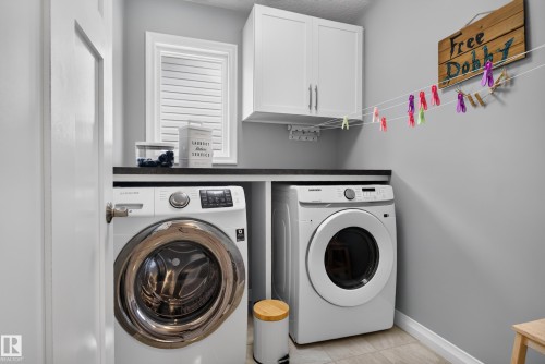 Dedicated laundry area featuring a window, built-in cabinetry, and a dark countertop - 22933 94A Avenue Nw, Edmonton, AB 
