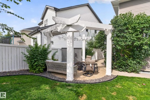 Expansive lawn with a white pergola, pea gravel patio, and surrounding mature landscaping - 22933 94A Avenue Nw, Edmonton, AB 