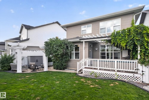 Expansive lawn with a white pergola, mature landscaping, and a multi-level deck with white lattice skirting - 22933 94A Avenue Nw, Edmonton, AB 