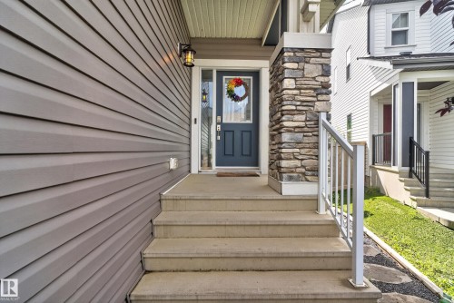 Entryway featuring concrete steps, a metal handrail, a stacked stone column, and gray horizontal siding - 22933 94A Avenue Nw, Edmonton, AB 