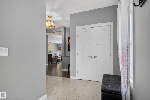 Tiled entryway flooring, white bi-fold doors with panel detailing, and a brass-finish semi-flush mount light fixture - 22933 94A Avenue Nw, Edmonton, AB 