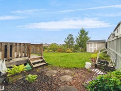 Expansive backyard featuring a wood deck with steps, a detached storage shed, a manicured lawn, and a planted garden bed - 