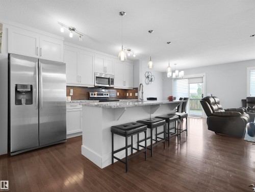 Kitchen featuring white cabinetry, stainless steel appliances, a center island with seating, and wood-finish flooring - 6656 Cardinal Rd Sw, Edmonton, AB 