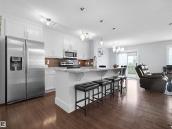 Kitchen featuring white cabinetry, stainless steel appliances, a center island with seating, and wood-finish flooring - 