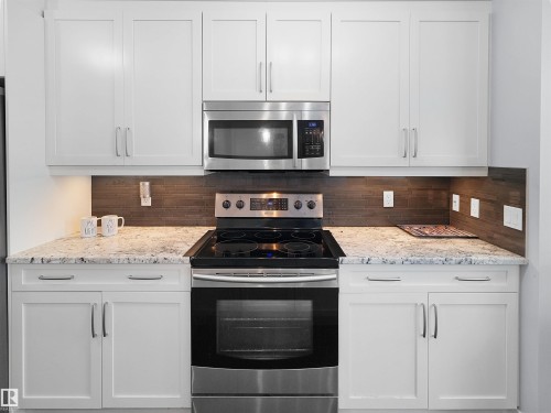 White shaker-style cabinetry, stainless steel appliances, speckled stone countertops, and a wood-finish tile backsplash - 6656 Cardinal Rd Sw, Edmonton, AB 