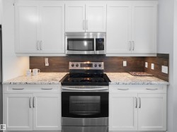 White shaker-style cabinetry, stainless steel appliances, speckled stone countertops, and a wood-finish tile backsplash - 