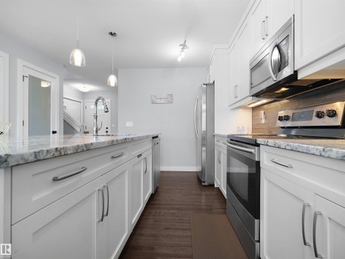 White shaker cabinetry with stainless steel hardware, wood-finish flooring, stainless steel appliances, speckled stone countertops, and a tile backsplash - 6656 Cardinal Rd Sw, Edmonton, AB 
