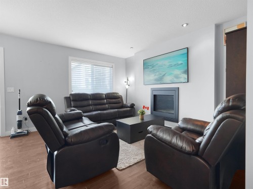 Wall-mounted fireplace with a black surround, wood-finish flooring, recessed lighting, and a large window with blinds - 6656 Cardinal Rd Sw, Edmonton, AB 