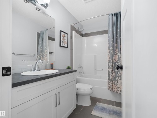 Bathroom featuring a white vanity with slab-panel doors, a dark countertop, an undermount sink, and a chrome faucet - 6656 Cardinal Rd Sw, Edmonton, AB 