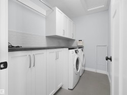 White cabinetry with silver-tone hardware, dark countertop, white subway tile backsplash, and light gray flooring - 
