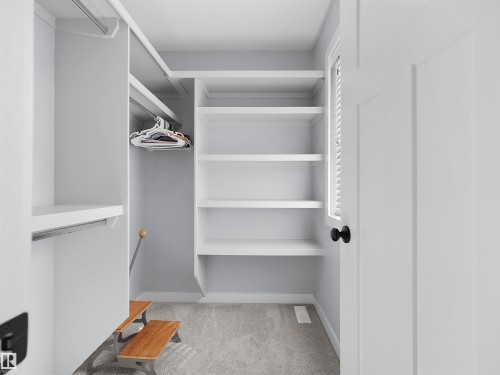 Custom closet system with built-in shelving, hanging rods, and light gray carpeting - 6656 Cardinal Rd Sw, Edmonton, AB 