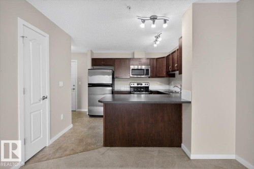 Kitchen featuring wood-finish cabinetry, stainless steel appliances, a dark countertop, and track lighting fixtures - #316 392 Silver Berry Rd Nw, Edmonton, AB - Indoor Photo Showing Kitchen