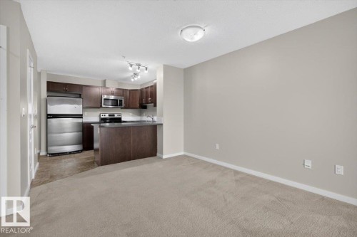 Open-concept living space featuring a full kitchen with stainless steel appliances, dark wood cabinetry, a breakfast bar, and tile flooring - #316 392 Silver Berry Rd Nw, Edmonton, AB - Indoor Photo Showing Kitchen