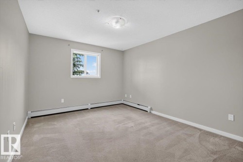 Carpeted room featuring light gray walls, a white-framed window, and a white baseboard heating system - #316 392 Silver Berry Rd Nw, Edmonton, AB - Indoor Photo Showing Other Room