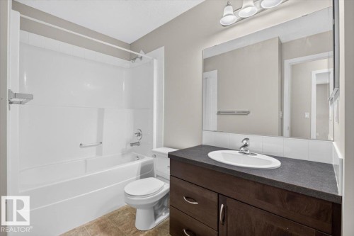 Bathroom featuring a dark wood-finish vanity with an integrated sink, a large wall-mounted mirror, a three-light fixture, and a bathtub with a shower surround - #316 392 Silver Berry Rd Nw, Edmonton, AB - Indoor Photo Showing Bathroom