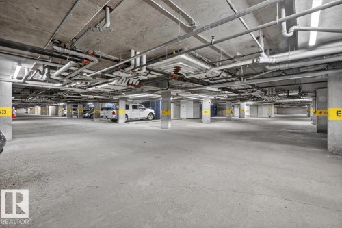 Concrete parking garage featuring exposed overhead piping and fluorescent lighting fixtures - #316 392 Silver Berry Rd Nw, Edmonton, AB - Indoor Photo Showing Garage