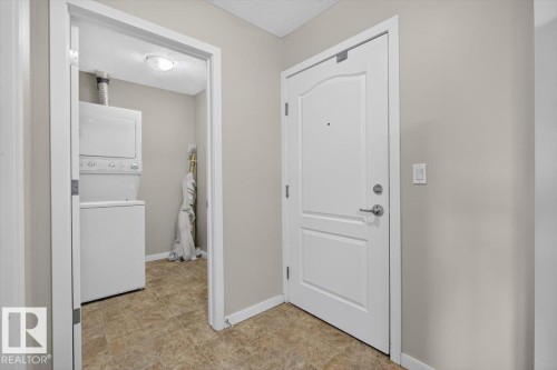 Entryway featuring a white paneled door with brushed nickel hardware, neutral painted walls, and textured floor tiles - #316 392 Silver Berry Rd Nw, Edmonton, AB - Indoor